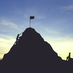 Two figures climb a hill towards a flag