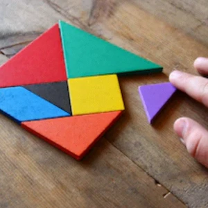 A close up of a person's hand solving a multi-coloured puzzle on a wooden table.