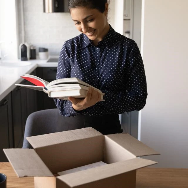 Smiling woman opening a box of books and reading one of them