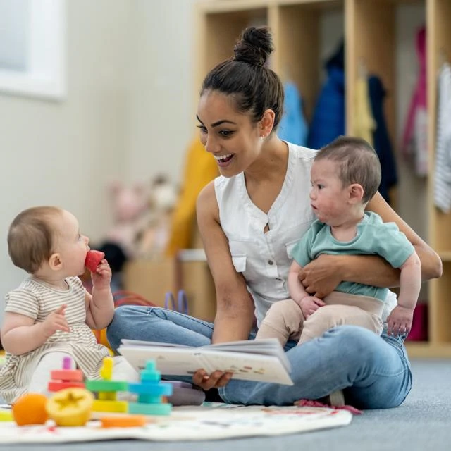 Femal member of staff reading a book to two babies