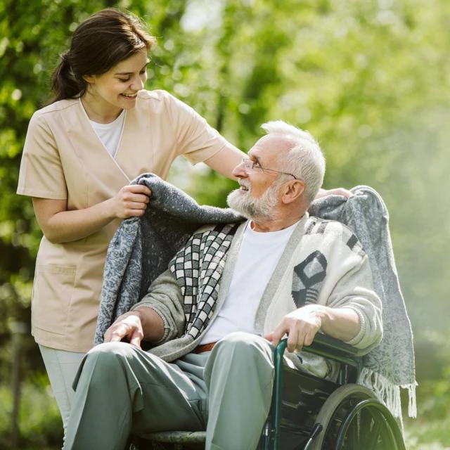 Care staff putting a blanket over the shoulders of a man in a wheelchair