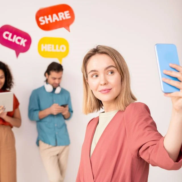 woman holding a smartphone and two people behind her viewing with the words click, share, hello in speech bubbles