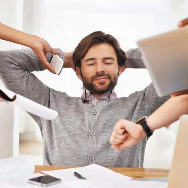 Male office worker with eyes closed and relaxed while colleagues are handing him a phone, a laptop and files