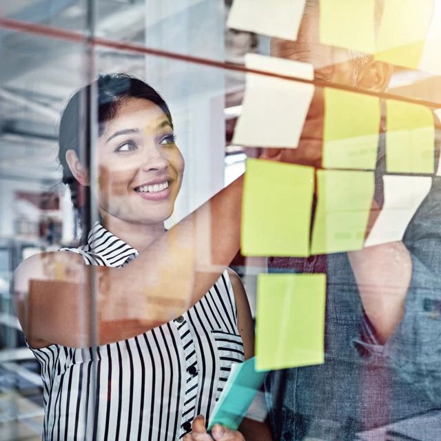 Woman smiling and looking at post it notes on glass wall
