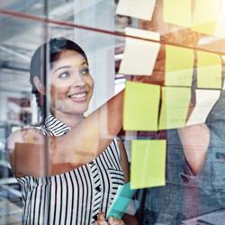 Woman smiling and looking at post it notes on glass wall