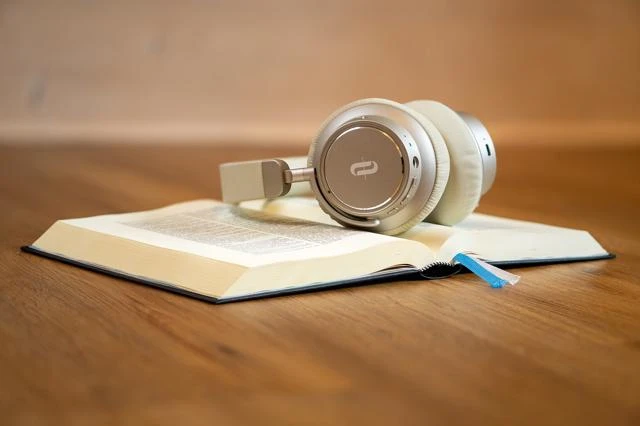 A book lies open on the table with a pair of headphones sitting on it