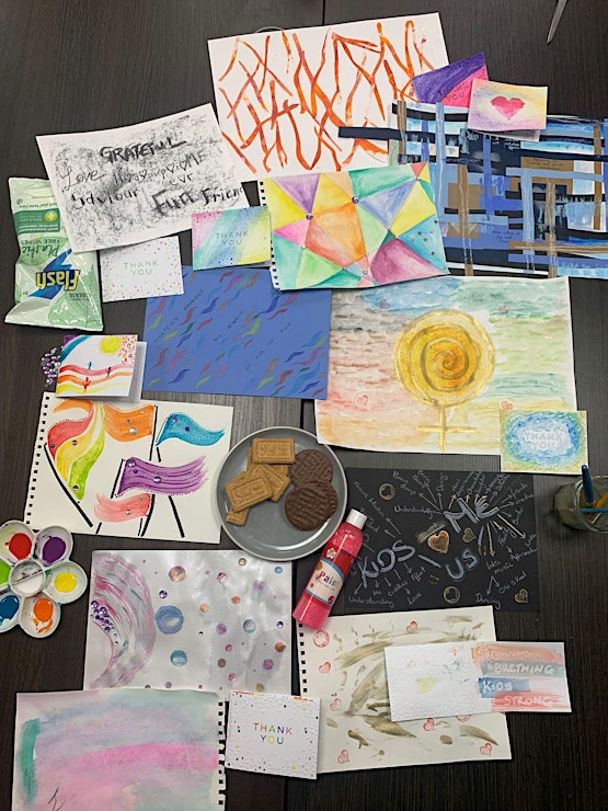 Colourful artworks spread on a table along with a plate of chocolate biscuits