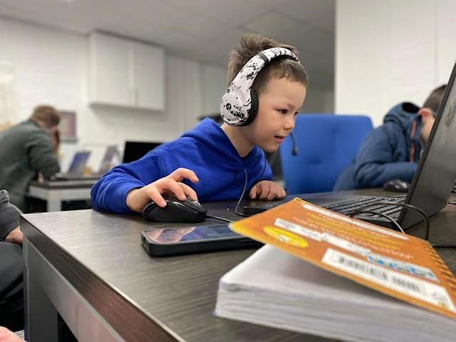 A boy wears headphones and uses a computer mouse