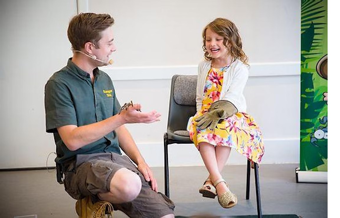 Ranger Stu holds a large spider and shows a smiling girl.