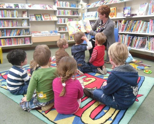 children sitting on a mat in a library listening to a story